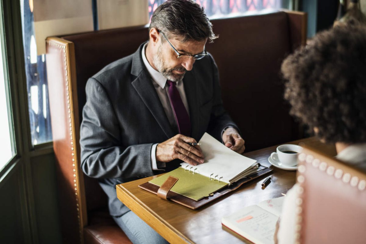 Advogado de terno analisa processo de cliente sentado em restaurante