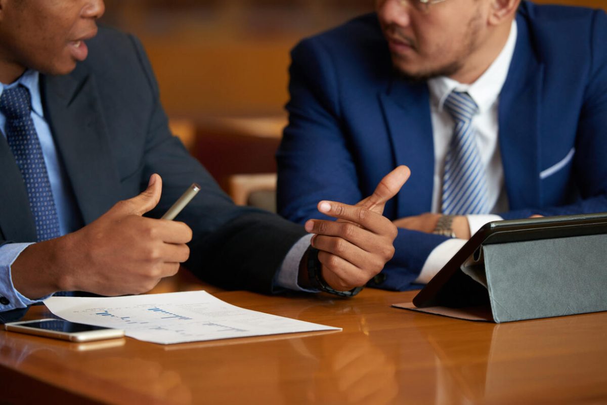 Dois advogados com ternos, caneta, papel e tablet discutem processo